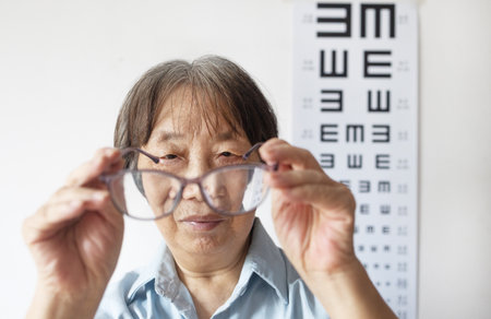 Asian senior woman wearing eyeglasses with eye chart in the background