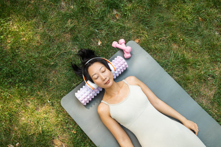 The Asian girl lies with her eyes closed, on a yoga mat, rest after training, appeasement,...