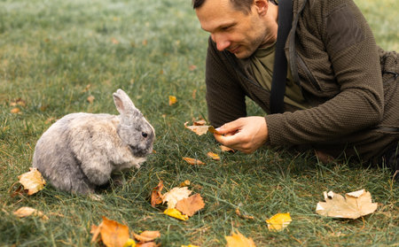 Young man feeding rabbit with autumn leaves in park. Selective focus.