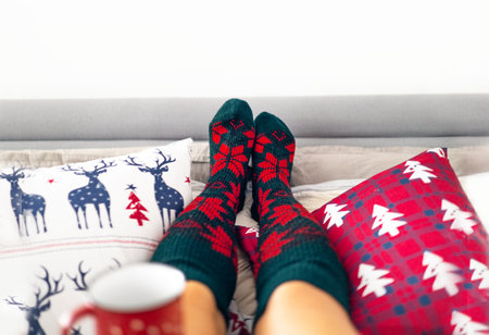 Feet in woollen socks in Christmas holidays. Woman relaxed on bed with coffee cup. Close up on feet. Winter and Christmas holidays concept.の写真素材