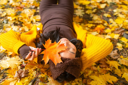 Young woman lying on the ground in autumn park with yellow maple leavesの写真素材