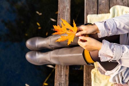Woman sitting on a pier and holding a yellow maple leaf in her handsの写真素材