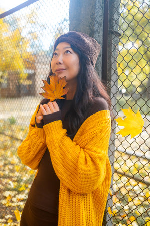 Portrait of a beautiful young brunette woman in a yellow sweater and hat on a background of autumn park.の写真素材