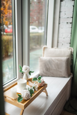 Cup of coffee on a wooden tray on window sill on cold autumn day. Cozy home with big window.の写真素材