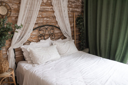 Details of bright elegant interior in cozy bedroom. Wicker side table with vase and flowers next to comfortable bed with white linen bedding.の写真素材