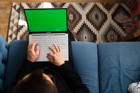 Man using a laptop with a green screen in the living room.の写真素材