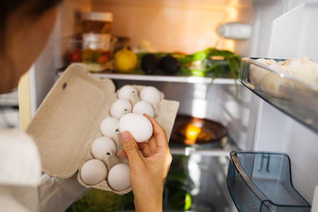 Close-up of woman taking chicken eggs out of fridge at nightの写真素材