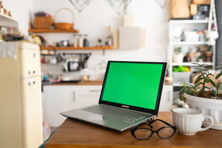 Laptop with green screen on wooden table in kitchen at home.の写真素材