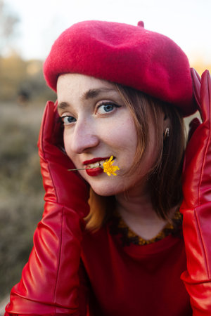 Young cute woman in red leather gloves and beret sitting on grass in autumn parkの写真素材
