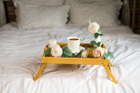 Wooden tray with hot coffee and flowers on bed at homeの写真素材