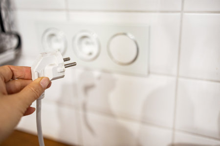 A woman's hand unplugging a power cord from an electrical outlet on a white wall.