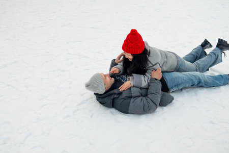 Loving couple in warm clothes lying on the snow and embracing and smiling. Romantic walking in snowy...