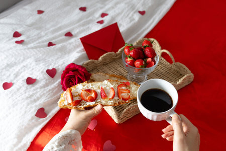 Breakfast in bed. Woman holds a cup with coffee. Breakfast with berries, heart, strawberries and croissant. Morning surprise. Valentine's Day. Honeymoon.の写真素材