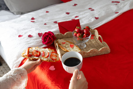 Breakfast in bed. Woman holds a cup with coffee. Breakfast with berries, heart, strawberries and croissant. Morning surprise. Valentine's Day. Honeymoon.の写真素材