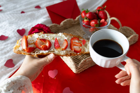 Breakfast in bed. Woman holds a cup with coffee. Breakfast with berries, heart, strawberries and croissant. Morning surprise. Valentine's Day. Honeymoon.の写真素材