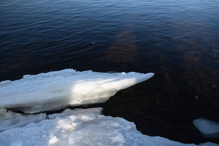 ice blocks illuminated by sun on the edge of clearing in frozen river in cold winter day.