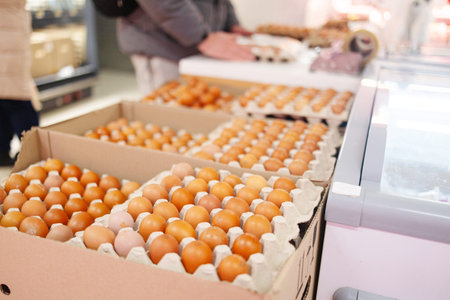 Stacked egg cartons filled with brown eggs on display, showcasing poultry farm produce ready for...