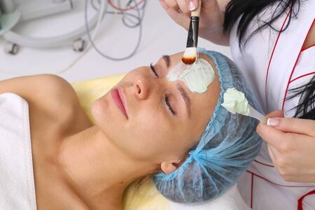 Cosmetician applying facial mask to the face of young beautiful woman in spa salonの写真素材