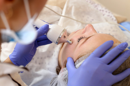 Close up of young woman receiving electric ultrasonic facial massage at beauty salon.の写真素材