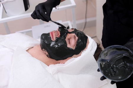Spa therapy for men receiving facial black mask.の写真素材