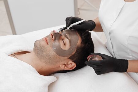 Beautician applying cosmetic mask on mans face in spa salon.の写真素材