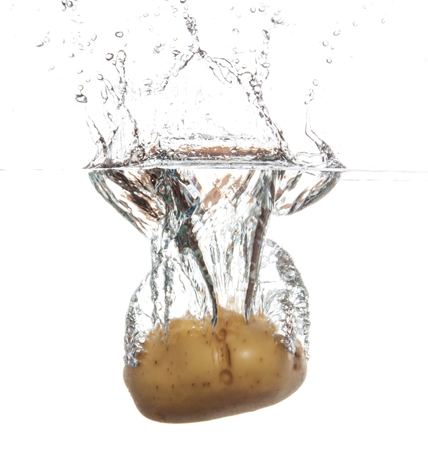 Potato splashing and sinking underwater. White beackgroung.の写真素材