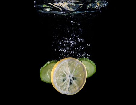 Slice of lemon and cucumber sinking underwaterの写真素材