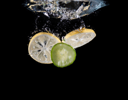 Slice of lemon and cucumber sinking underwaterの写真素材