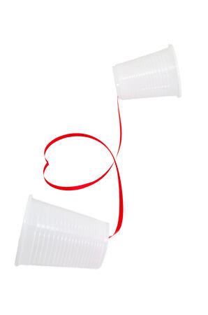 Long distance relationship concept. 2 white plastic cups connected with a red threadの写真素材