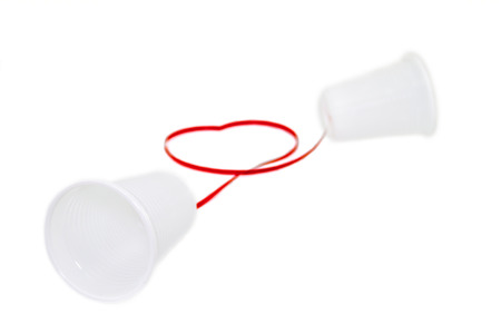Long distance relationship concept. 2 white plastic cups connected with a red threadの写真素材