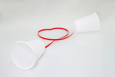 Long distance relationship concept. 2 white plastic cups connected with a red threadの写真素材
