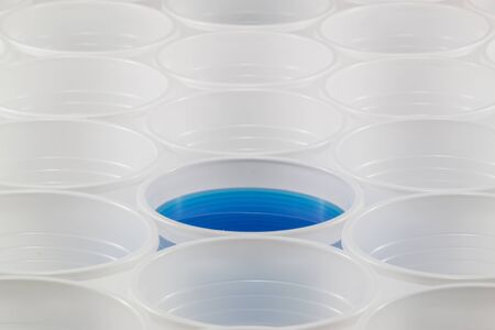 Lots of white plastic cups. One cup filled with blue water. Shallow depth of field.の写真素材