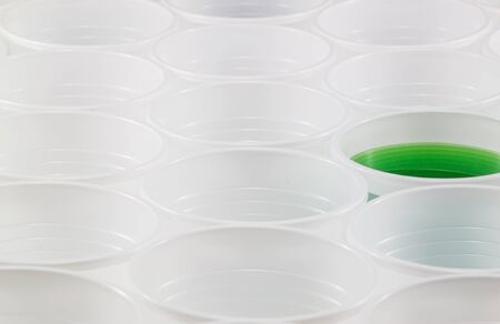 Lots of white plastic cups. One cup filled with green water. Shallow depth of field.の写真素材