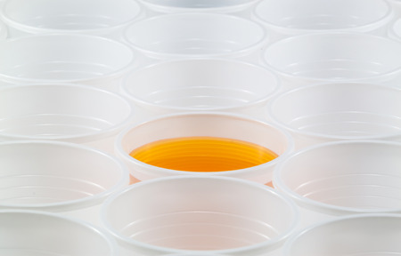 Lots of white plastic cups. One cup filled with yellow water. Shallow depth of field.の写真素材