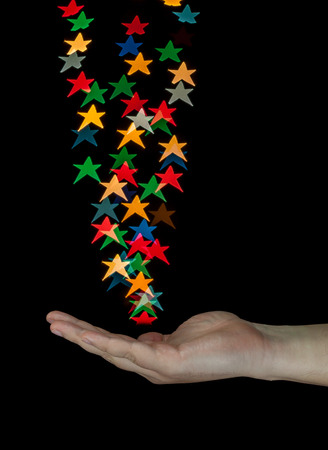 Human hand catching star shaped bokeh created from decoration lights. Isolated on black background.の写真素材