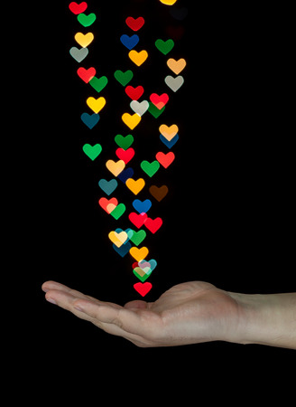 Human hand catching heart shaped bokeh created from decoration lights. Isolated on black background.の写真素材