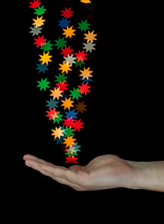 Human hand catching star shaped bokeh created from decoration lights. Isolated on black background.の写真素材
