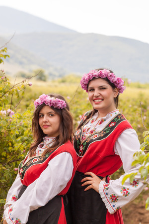 Women dressed in a Bulgarian traditional folklore costume picking roses in a garden, as part of the summer regional ritual in Rose valley, Bulgaria.の写真素材