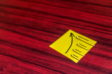 Paper clips attached by size on a yellow note with an arrow written on it.の写真素材
