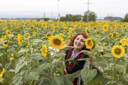 Girl in a traditional Bulgarian dress feeling happy in a field of sunflowersの写真素材