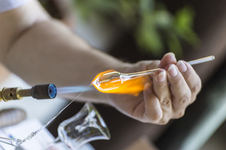 Craftsman melting and shaping a piece of glass on a small blue torchの写真素材