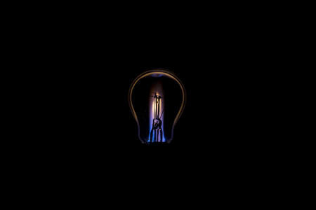 Tungsten light bulb burning like a candle isolated on black background.の写真素材