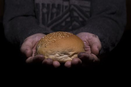 Poverty concept. Dirty hands giving bread isolated on balck background.の写真素材