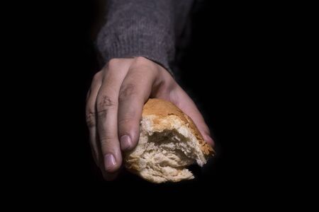 Poverty concept. Dirty hands giving bread isolated on balck background.の写真素材
