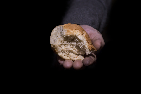 Poverty concept. Dirty hands giving bread isolated on balck background.