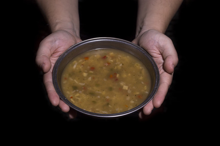 Poverty concept. Man holding a metal bowl of soup isolated on black background.の写真素材