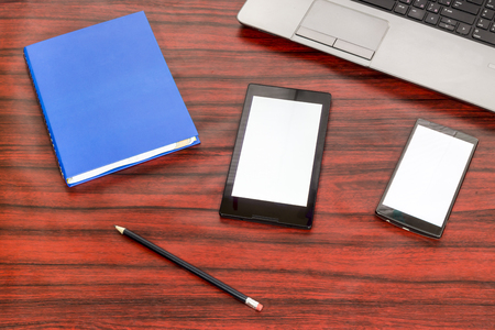 Book, tablet and cellphone laying next to a laptop and pencil on a desk.の写真素材