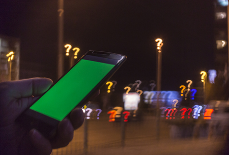 Searching in the city concept. Hand holding phone with green screen and question mark bokeh in the backgroundの写真素材