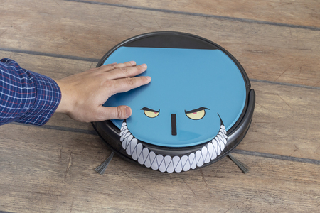 Hand petting a robot vacuum cleaner. Evil robots and takeover concept.の写真素材