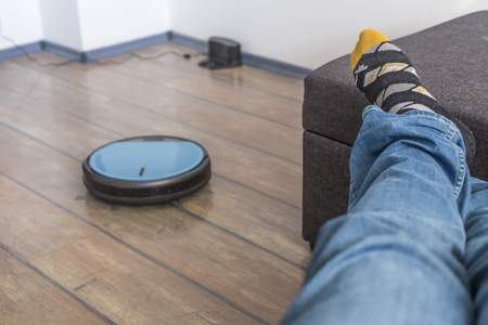 Man laying on a couch holding a looking at a robot vacuum cleanerの写真素材